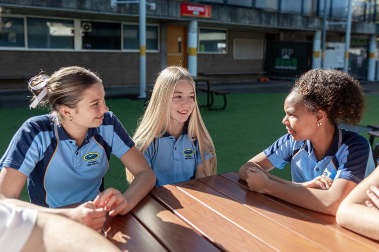 three female students sitting at a table looking at each other